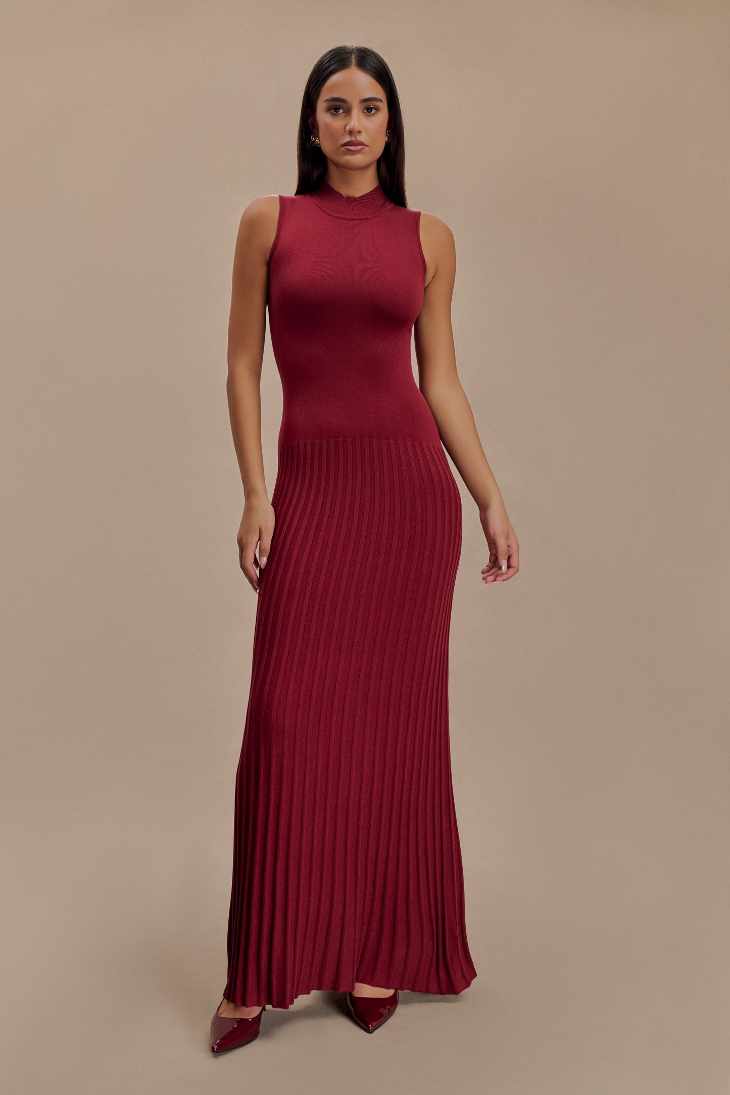 Vrouw draagt de Selena bordeauxrode plissé maxi jurk in een klassieke setting