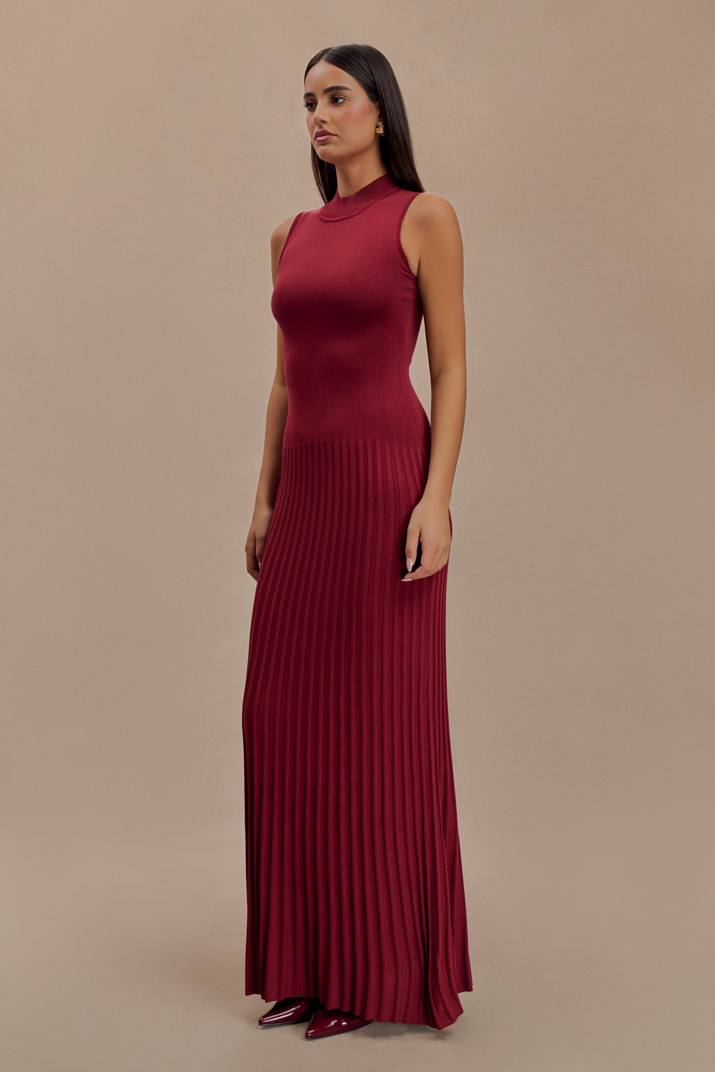 Vrouw draagt de Selena bordeauxrode plissé maxi jurk in een klassieke setting