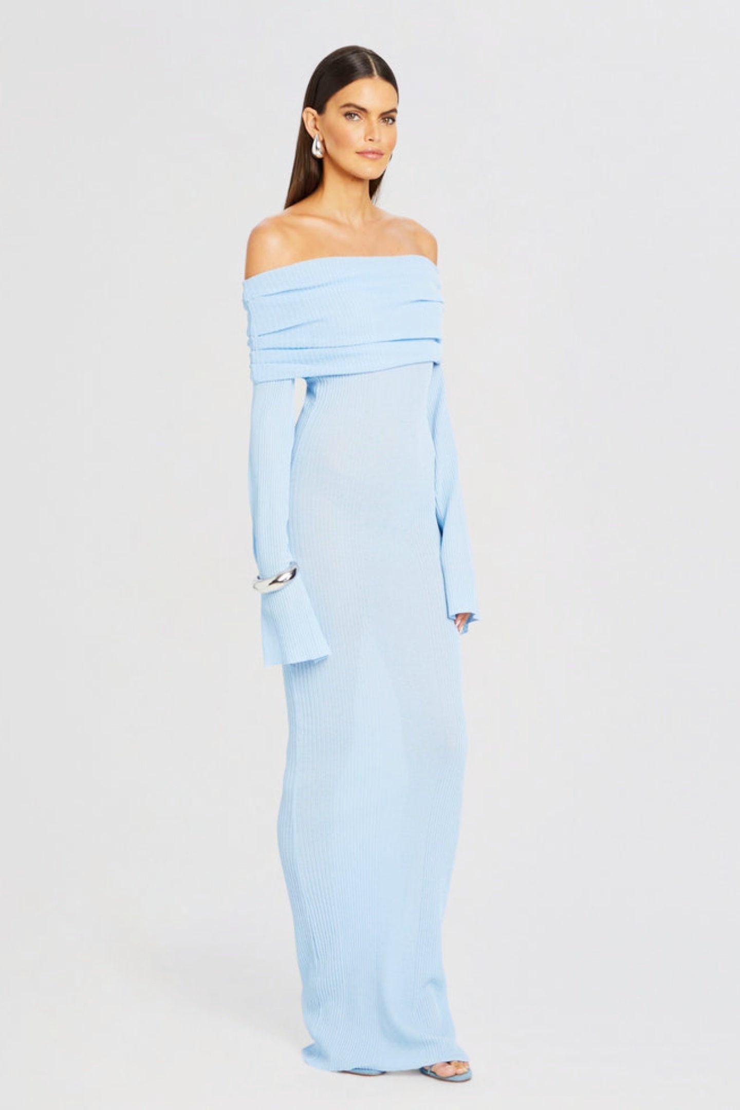 Vrouw draagt de Marina off-shoulder maxi jurk in blauwe kleur met lange mouwen