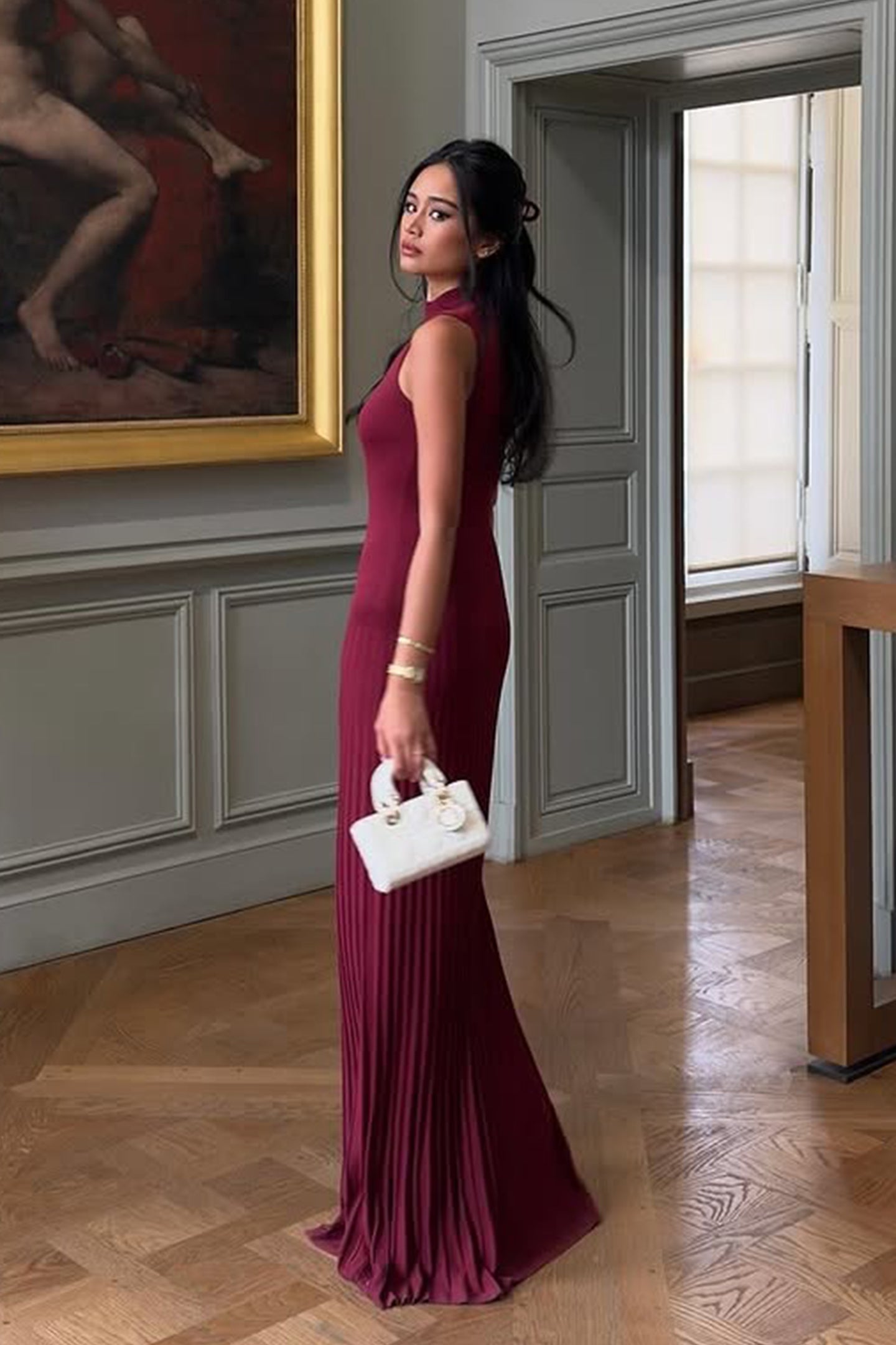 Vrouw draagt de Selena bordeauxrode plissé maxi jurk in een klassieke setting