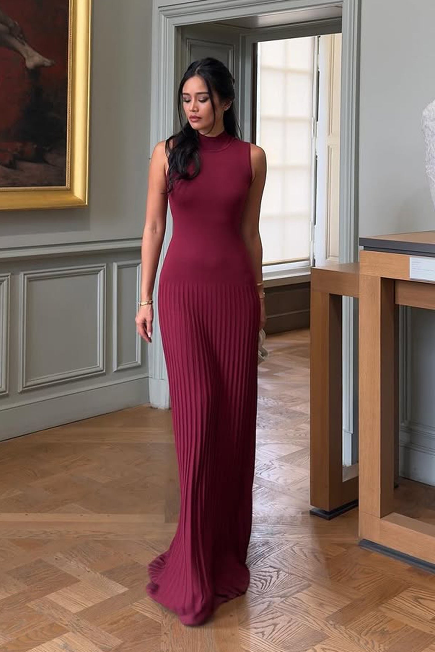 Vrouw draagt de Selena bordeauxrode plissé maxi jurk in een klassieke setting