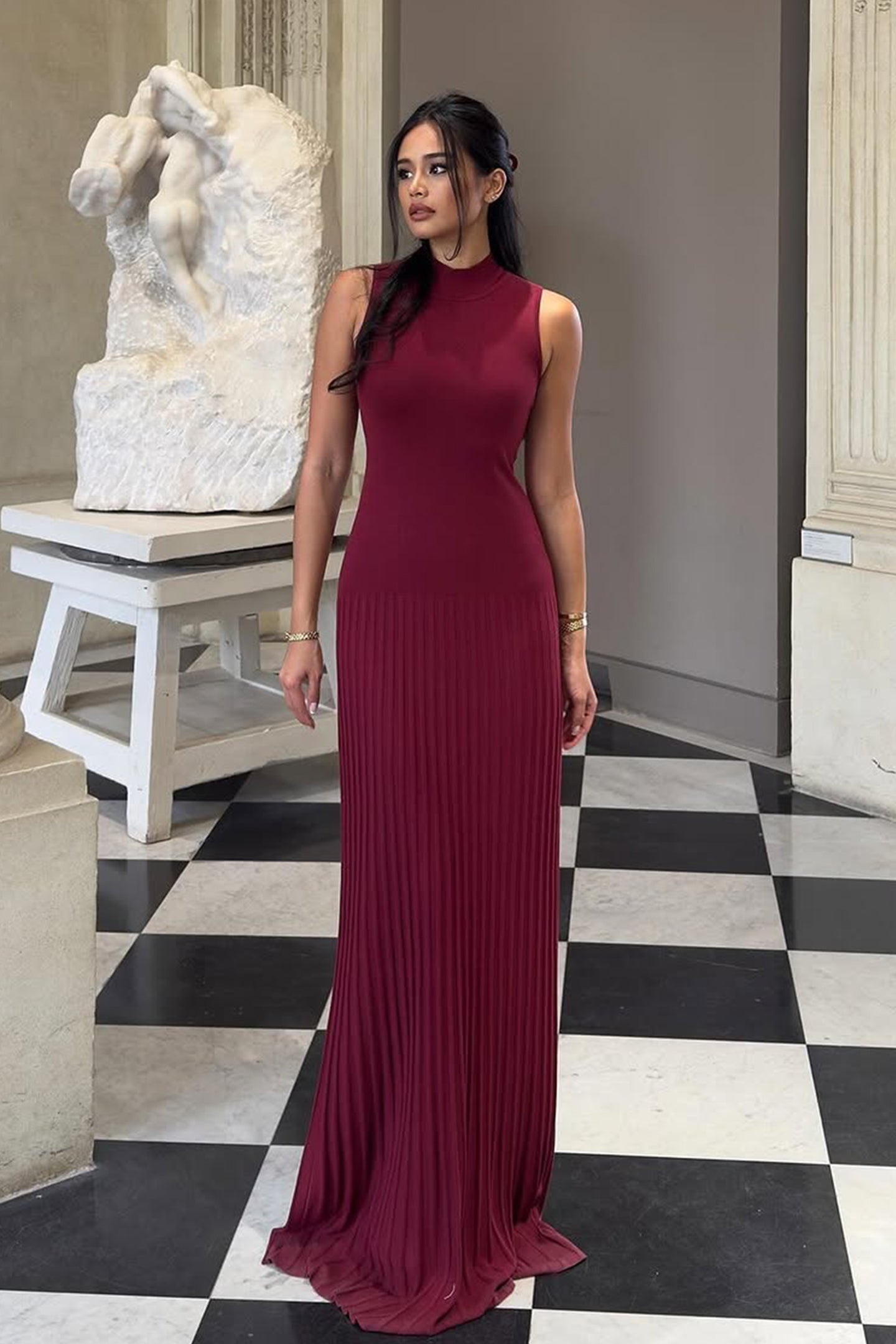 Vrouw draagt de Selena bordeauxrode plissé maxi jurk in een klassieke setting