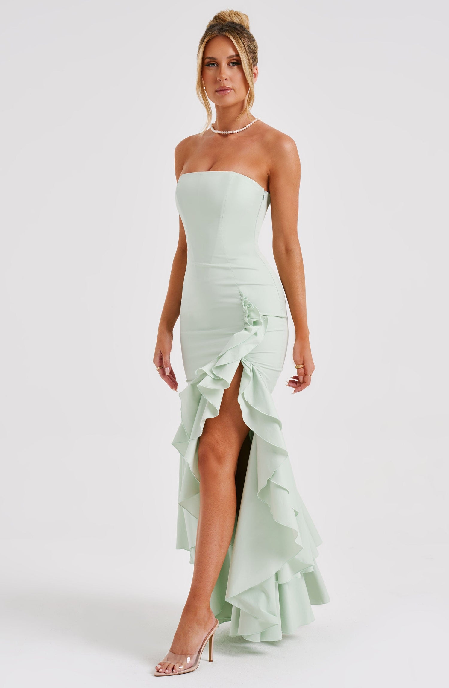 Stijlvolle vrouw in een strapless wit-blauw gestreepte maxi jurk, ontspannen op een bank met schoenen uit