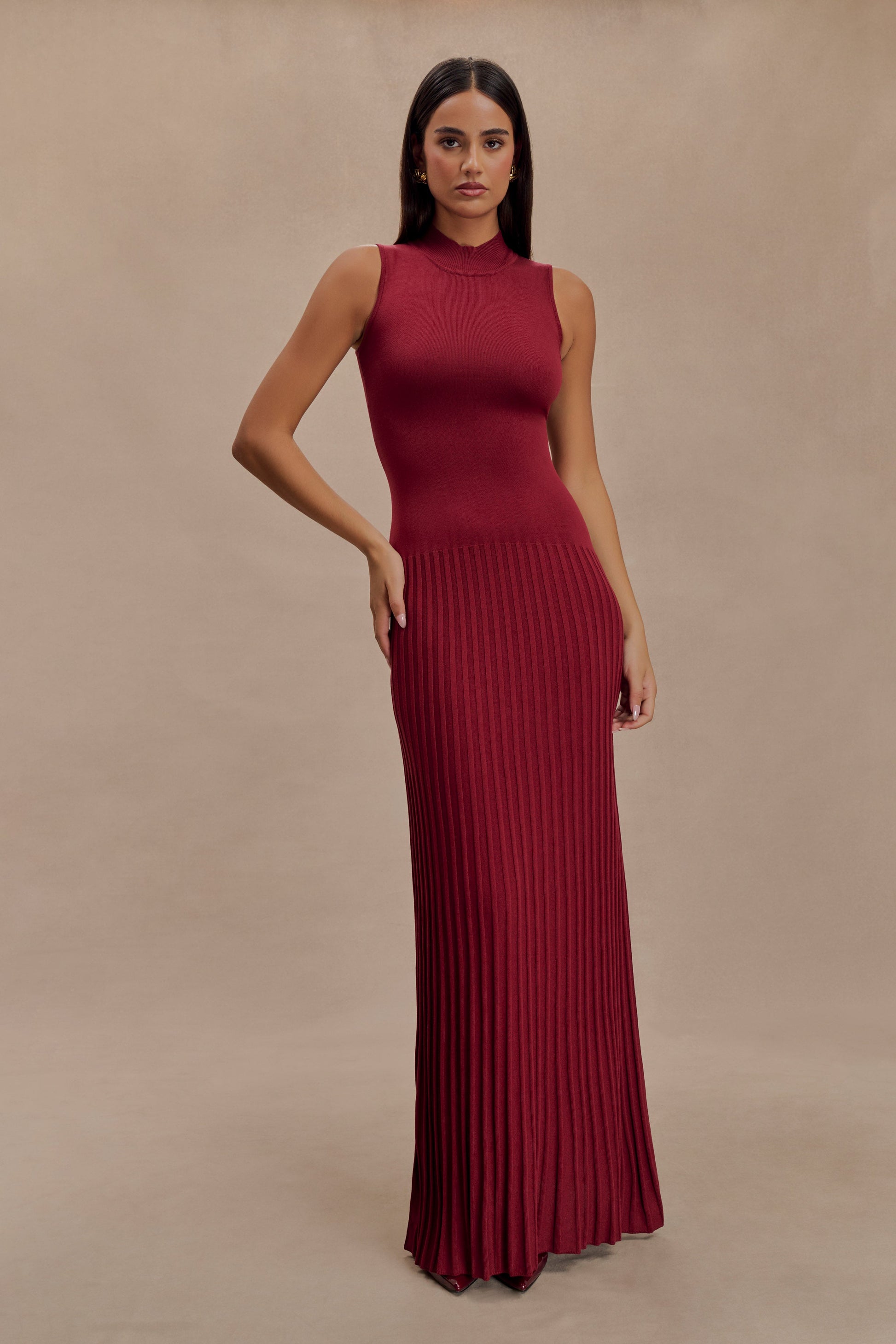 Vrouw draagt de Selena bordeauxrode plissé maxi jurk in een klassieke setting