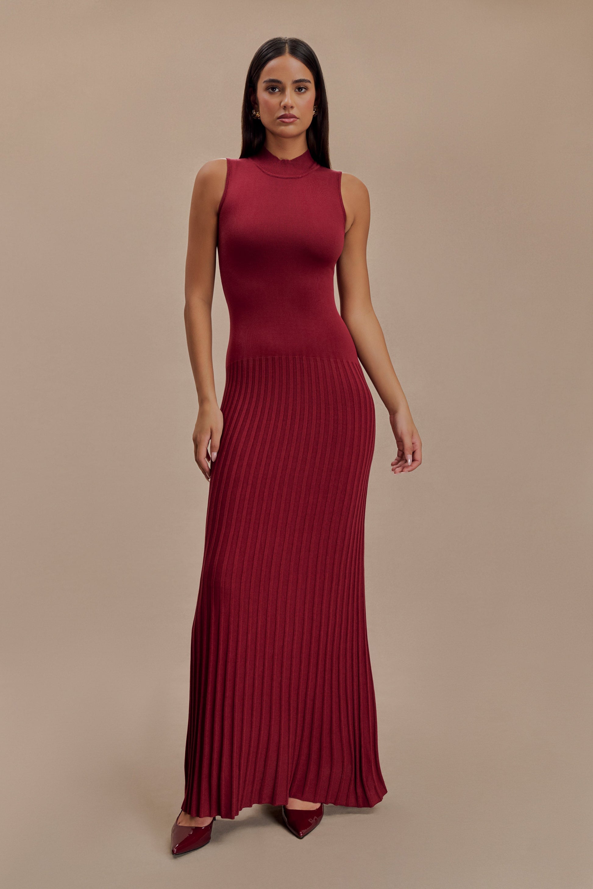 Vrouw draagt de Selena bordeauxrode plissé maxi jurk in een klassieke setting