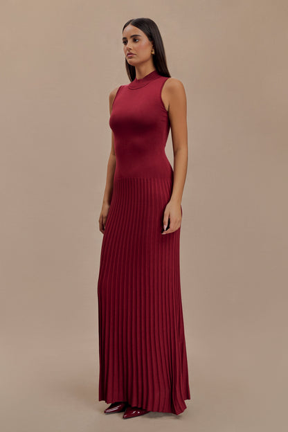 Vrouw draagt de Selena bordeauxrode plissé maxi jurk in een klassieke setting