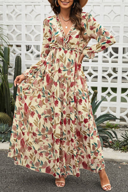 Vrouw draagt een roze bloemen maxi-jurk met rode en groene accenten, V-hals en lange mouwen, geschikt voor feest en vakantie