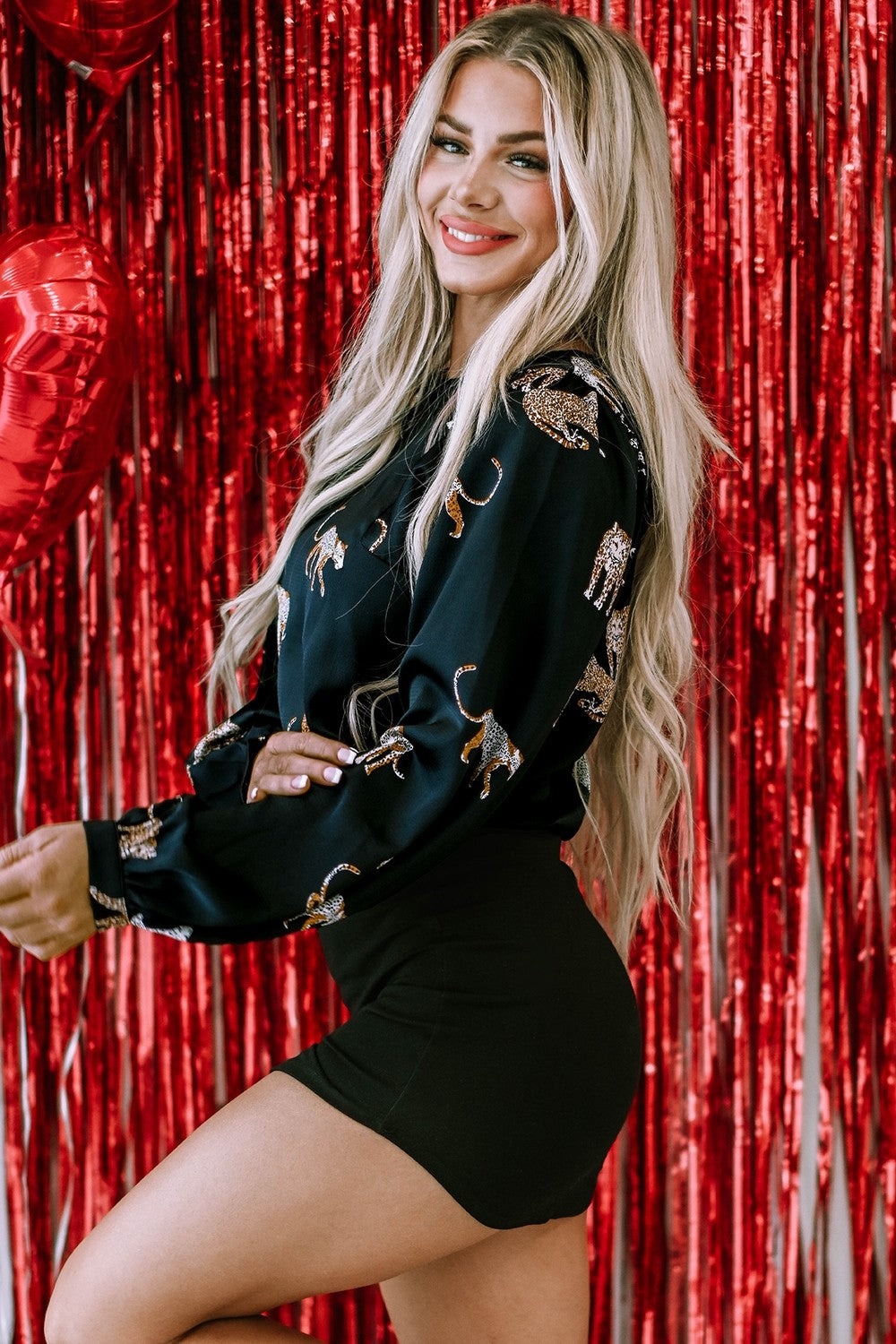 Vrouw draagt zwarte blouse met panterprint en ballonmouwen, gecombineerd met zwarte rok.
