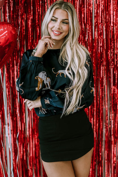 Vrouw draagt zwarte blouse met panterprint en ballonmouwen, gecombineerd met zwarte rok.